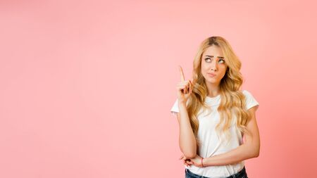 Let me think. Doubtful woman having idea, holding finger up over pink background. Panorama with empty spaceの写真素材