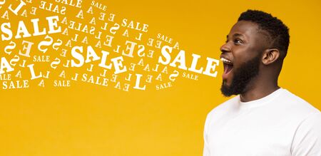 Emotional afro man screaming sale at copy space on yellow background, alphabet letters flying out of his mouth, panoramaの写真素材