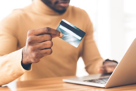 Money Transfer. Unrecognizable african guy holding plastic credit card and using laptop. Copy spaceの写真素材