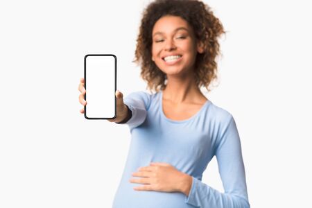 Pregnancy applications. Afro lady showing cellphone with empty screen over white background