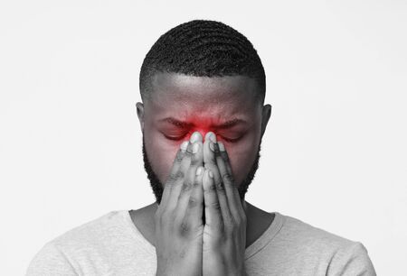Monochrome photo of black guy with closed eyes touching his nose, having sinus pain, highlighted red zoneの写真素材