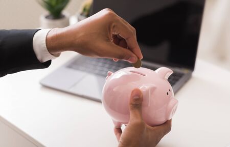 Cropped of black businessman holding piggy bank, putting coins in it, finance and banking conceptの写真素材