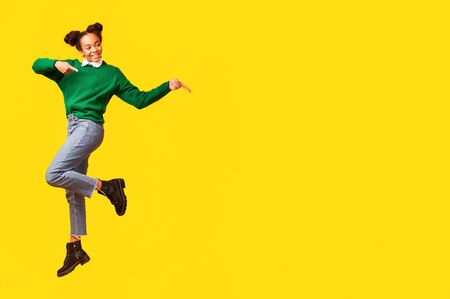 Look At It. Happy black girl jumping on air and pointing aside. Copyspace, full lengthの写真素材