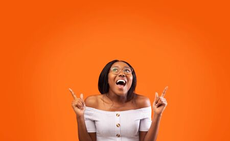 Look There. Excited Afro Lady Pointing Fingers Up At Empty Space Standing Over Orange Background. Studio Shotの写真素材