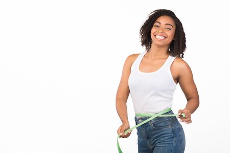 Weight Loss. Happy afro woman measuring her waist using tape after fitness exercise, smiling at...