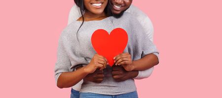 Cropped image of afro couple holding red heart shaped card together over pink background, panorama...