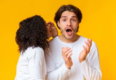 African American Girl Sharing Secret With Her Boyfriend. Surprised Guy Opened Mouth In Surprise,...