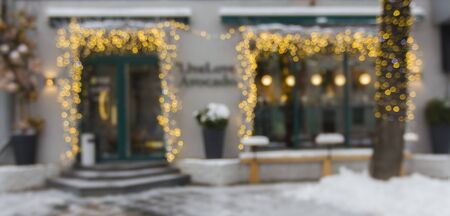 Winter decorations. Blurred cafe facade with lights and snowy asphalt, panorama, copy spaceの写真素材