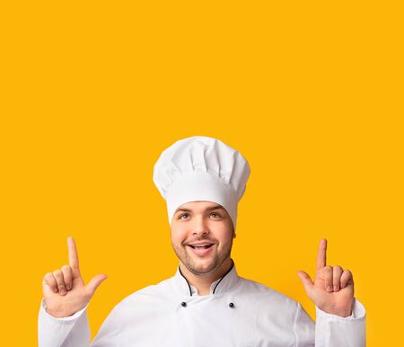 Look There. Smiling Chef Man Pointing Fingers Up At Copy Space Over Yellow Studio Background.の写真素材