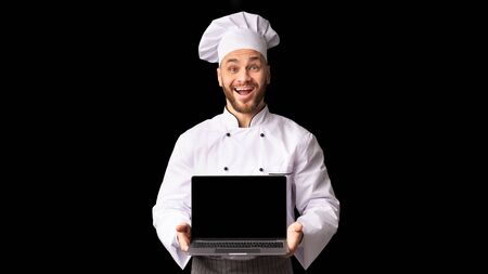 Cooking Food Online Courses. Excited Chef Man Holding Laptop With Blank Screen Recommending Culinary Website Standing On Black Background. Panoramaの写真素材