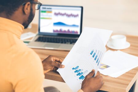 Busy Day. Rear view of afro trader working with charts and market reports on computer screen in...