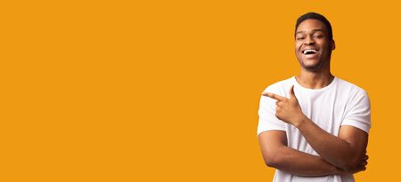 Advertisement Concept. Happy black guy pointing at copy space isolated over yellow studio...