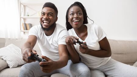 Joyful african american couple competing with each other in video game, holding joysticks and...
