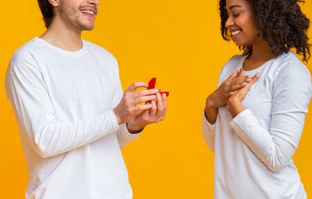Surprising Proposal. Shocked Black Girl Looking At Engagement Ring That Boyfriend Giving Her Over Yellow Background, Cropの写真素材