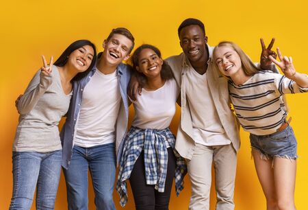 Group of international cheerful students smiling and embracing over yellow studio backgroundの写真素材