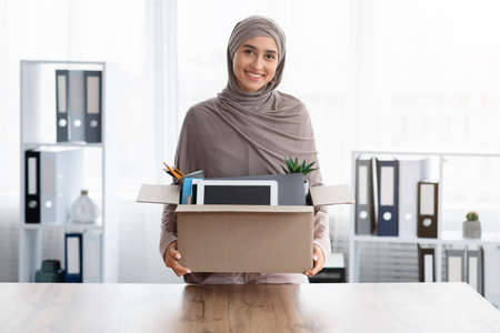First Day In New Office Concept. Happy Muslim Female Employee Holding Box With Her Belongings, Moving To New Workplace, Got Promotion, Free Spaceの写真素材