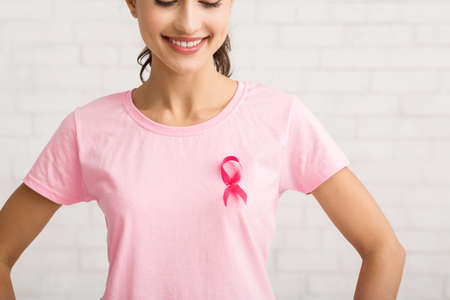Breast Cancer. Unrecognizable Girl With Awareness Ribbon On Pink T-Shirt Standing Over White Brick Wall Background. Croppedの写真素材