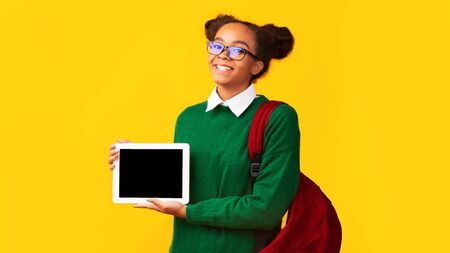 Cool App. Young black teenage girl showing blank tablet computer screen at studio. Panorama, empty space, mock upの写真素材