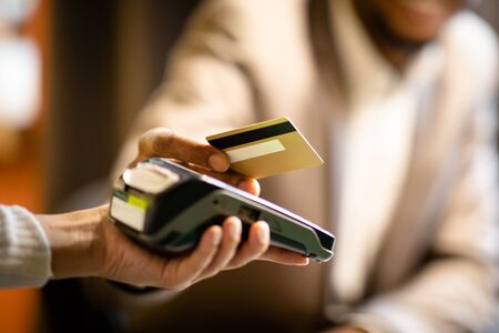 Unrecognizable afro businessman in suit giving credit card to barman paying with gold credit card in...