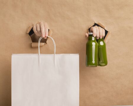 Healthy green juice detox smoothie and female hands holding paper bag with copy space for ad, cardboard backgroundの写真素材