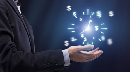 Time is money concept. Businessman's hand holding virtual clock with dollar sign icons, standing over dark background, side view, panoramaの写真素材