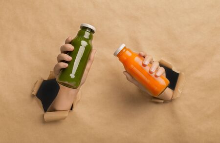 Power of healthy lifestyle. Female holding orange and green detox drink in hands through cardboard wall backgroundの写真素材