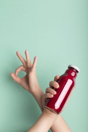 Say ok to healthy lifestyle. Glass bottle with red beet detox drink in woman hand over green background, copy spaceの写真素材