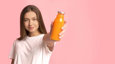 Detox concept. Fit, beautiful, young woman holding a healthy, orange smoothie or juice, on pink background, panorama, copy spaceの写真素材