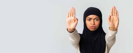 Refusal Concept. Serious afro islamic girl in headscarf making stop hand gesture with opened palms, standing over light gray background, panoramaの写真素材