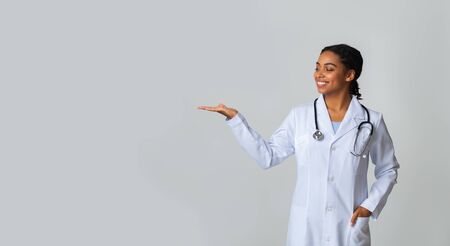 Medical Ad. Afro Female Doctor Holding And Looking At Some Invisible Object On Her Palm, Standing With Extended Hand Over Light Background, Panoramaの写真素材
