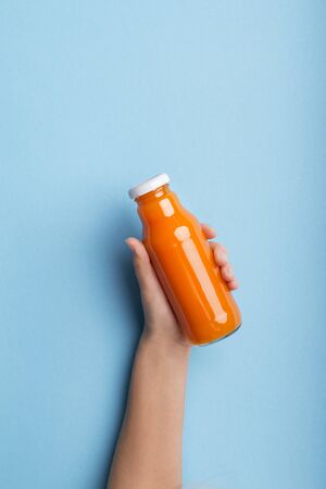 Healthy lifestyle concept. A bottle of orange juice or detox drink in a womans hand over blue background, copy spaceの写真素材