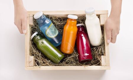Healthy vibes. Female holding wooden box with Different flavoured detox drinks in glass bottles on white backgroundの写真素材