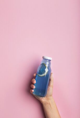 A bottle of blue water or detox drink in a woman's hand over pink background, copy space. Concept of healthの写真素材