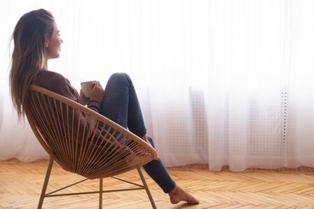 Harmony of life. Calm woman with coffee enjoying moment, looking at window, free spaceの写真素材