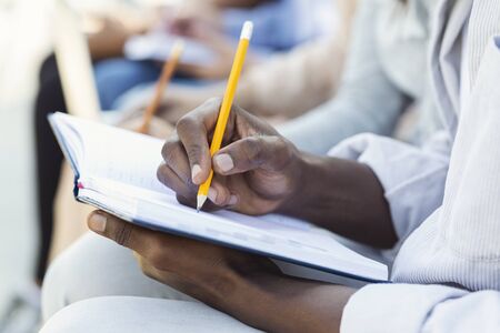 Cropped of black student guy taking notes, studying with friends, using notepad and pencil