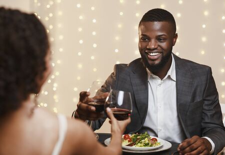Happy afro man in suit toasting with his girlfriend in restaurant, having valentine dinner