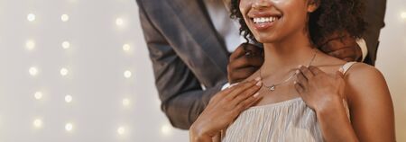 Gift for Valentine's Day. Cropped of african man putting beautiful necklace on woman neck, panorama with free spaceの写真素材
