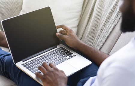 African american man browsing on laptop, sitting on couch at home, empty space