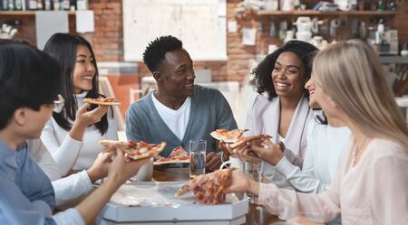 Multiracial colleagues eating pizza and having fun, office interiorの写真素材