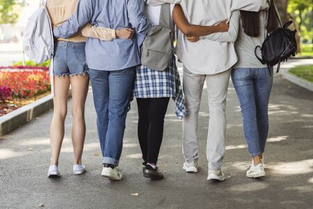 Cropped of teen international friends hugging and walking by street, back view, friendship concept