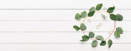 Wedding traditions. Creative flat lay of gold rings with green leaves on wooden background,...