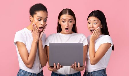 Three Surprised Millennial Girls Looking At Laptop Browsing Internet Standing On Pink Background. Studio Shotの写真素材