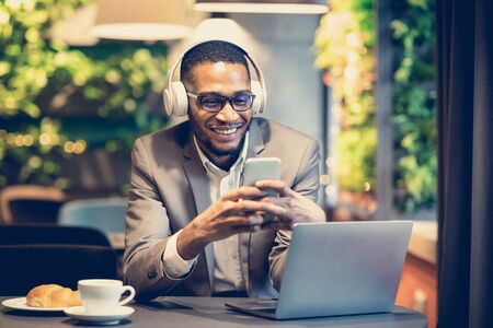 Lifestyle Concept. Young afro man texting message on smart phone, listening to music in headphones...