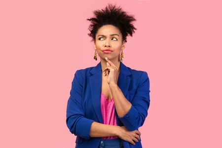 Pensive afro woman looking up, touching her chin, isolated over pink studio wall, copyspaceの写真素材