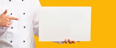 Unrecognizable Chef Man Pointing Finger Showing Blank White Poster Over Yellow Studio Background....