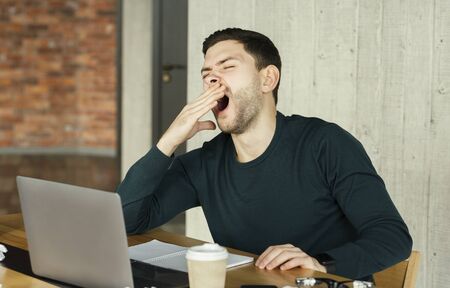 Sleepy Office Guy Yawning At Laptop Sitting At Workplace Indoor. Work Exhaustion. Selective Focusの写真素材