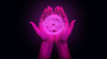 Occultism Concept. Two female open palms holding neon pentagram framed with circle over black backgroundの写真素材