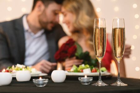 Valentines Day Celebration. Romantic Couple Having Dinner In Restaurant, Two Champagne Glasses Standing On Table In Foreground, Selective Focusの写真素材