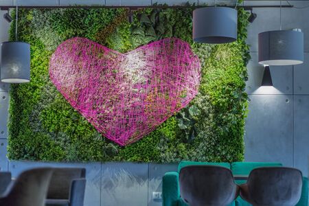 Romantic atmosphere on Saint Valentine's Day. Coffee shop or cafe interior with green plant wall and pink heart for photo zone, copy spaceの写真素材