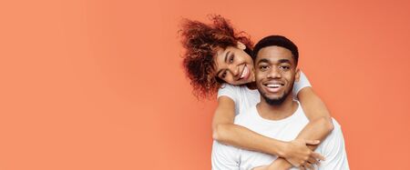 Loving African American Couple Cuddling Hugging Posing Over Orange Studio Background. Panorama With...